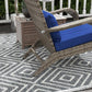 Wicker lounge chair with blue seat cushion and matching ottoman, side view