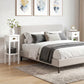 White 2-tier nightstand-style side table with drawer and open shelf beside a bed.