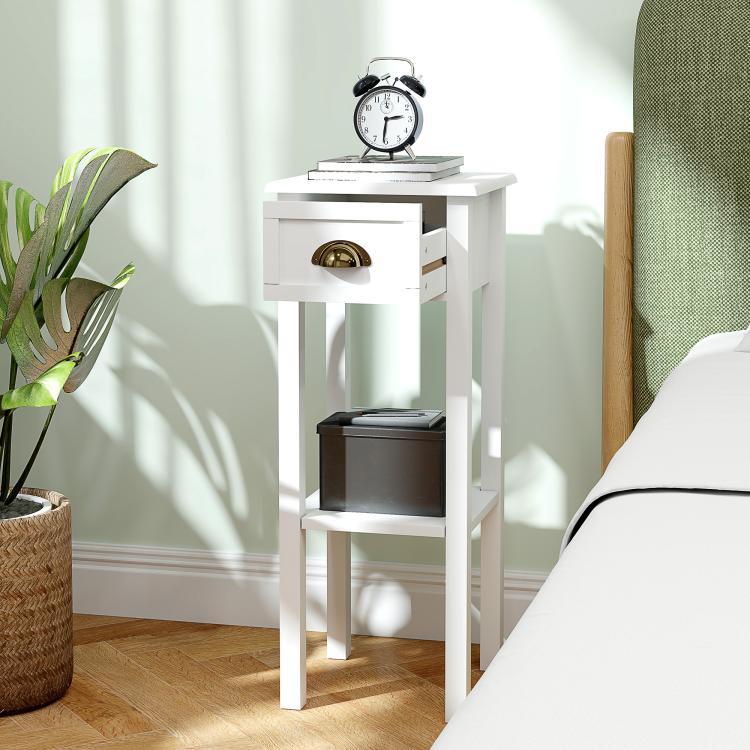 White 2-tier side table with drawer and open shelf next to a sofa and plant pot.