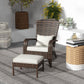 Brown wicker chair with white cushion seat and ottoman beside outdoor side table