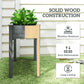 Elevated dark gray wooden planter box with solid wood-style legs and planted greens