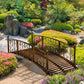 Bronze metal arched garden footbridge with scroll railings in a landscaped yard
