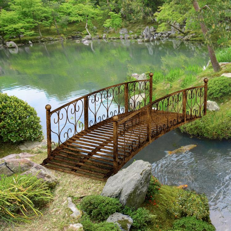 Bronze metal arched garden footbridge over a pond with scroll side railings