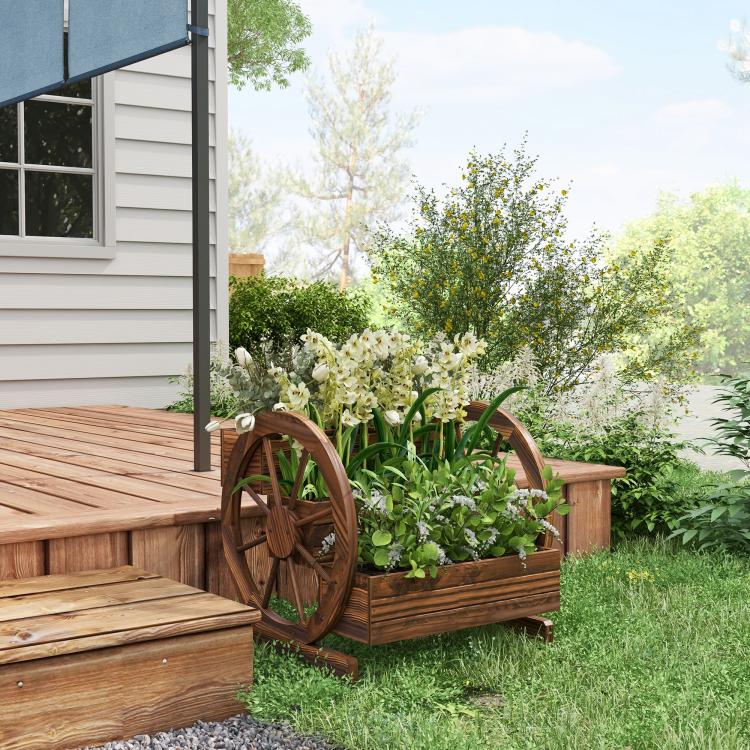 Wooden wagon planter box with wheel accents, holding white flowers near a house