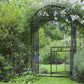 Grey metal garden arbor arch with double doors open, framed by greenery and flowers