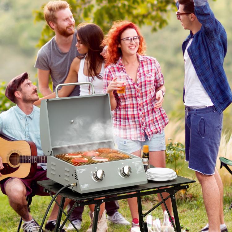 2-burner tabletop gas grill on outdoor table with lid open and food inside