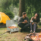 Folding 2-burner gas grill beside campfire, lid closed on stable legs