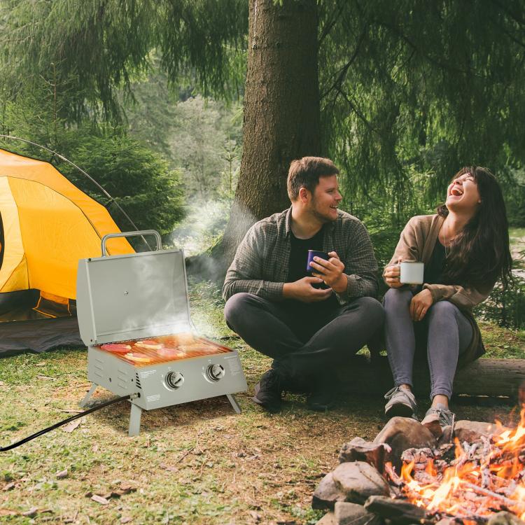 Folding 2-burner gas grill beside campfire, lid closed on stable legs