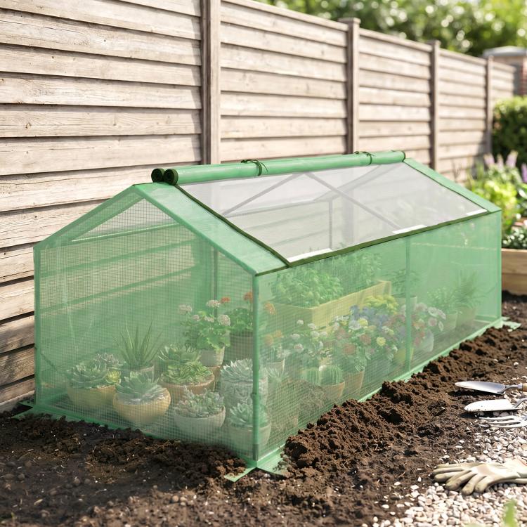 Green mini greenhouse in a garden bed with transparent mesh walls and roof