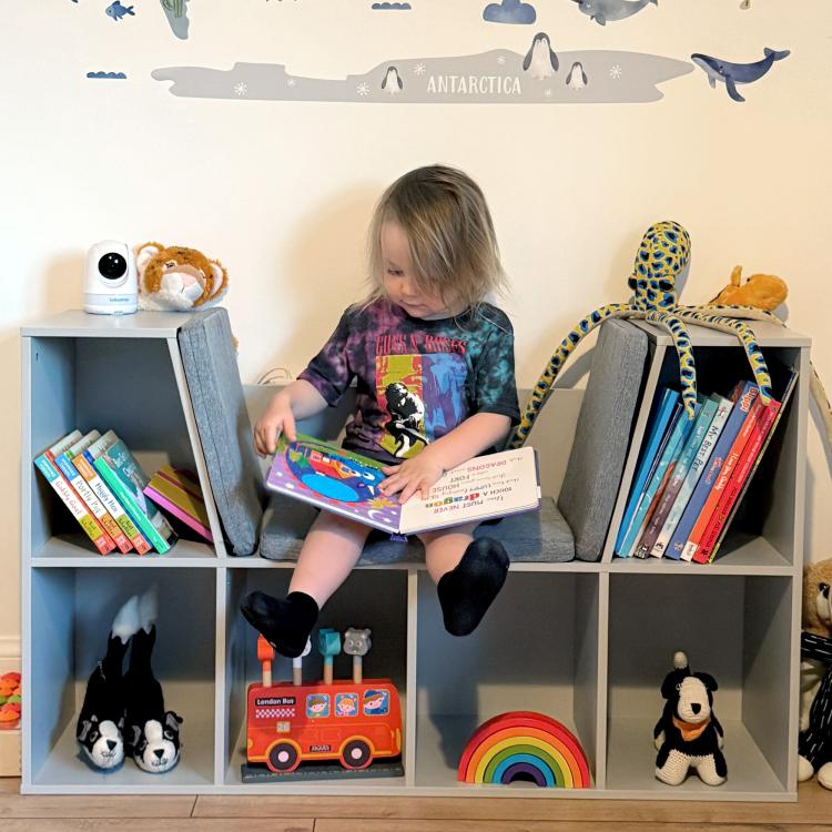 Children seated with a book on the cushioned reading nook of a grey cubby bookcase