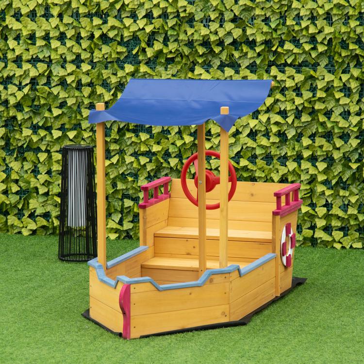 Boat-style kids wooden sandbox with blue canopy and red wheel at play station