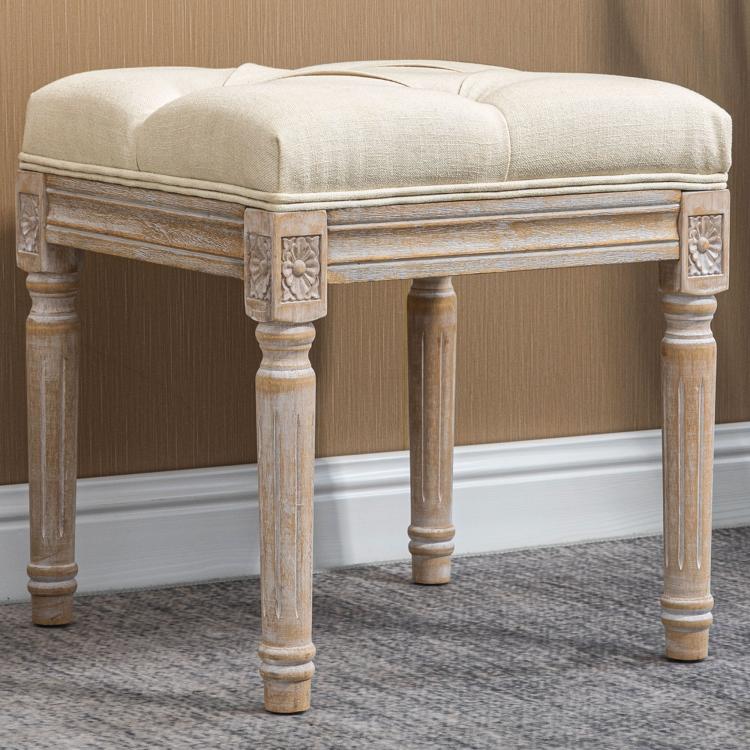 Beige upholstered ottoman bench with button-tufted seat and carved wooden legs