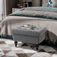 Gray storage ottoman with lid open, tufted top, nailhead trim, and turned legs