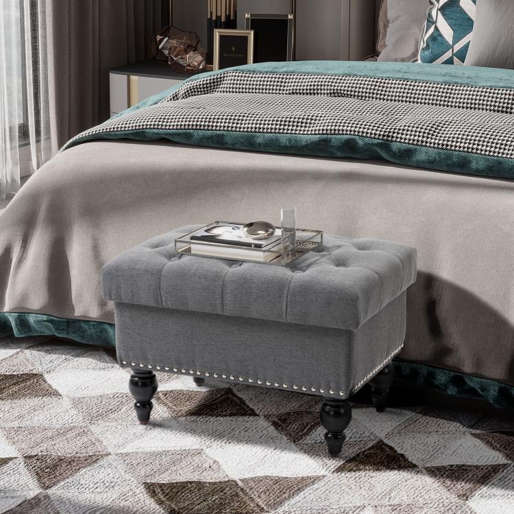 Gray storage ottoman with lid open, tufted top, nailhead trim, and turned legs