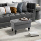Gray storage ottoman with tufted seat, nailhead trim edge, and turned legs