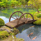 Stained wooden garden footbridge spanning a pond with wheel-style arched railings