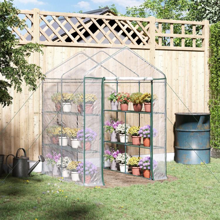Clear mini walk-in greenhouse with green frame and multi-tier shelving in backyard