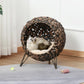 Woven round cat bed with raised tripod legs and cream cushion, cat inside