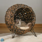 Brown woven cat condo with cream cushion and raised legs, cat resting inside