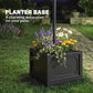 Square planter base with dark finish holding flowers next to solar lamp post light
