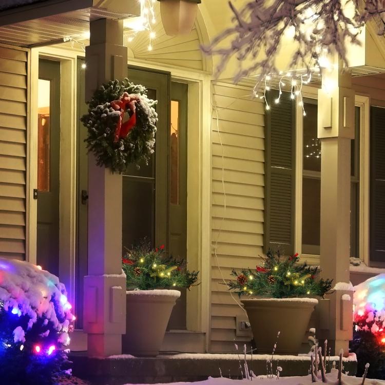 Pre-lit artificial Christmas tree set on porch steps with warm white lights and red berries