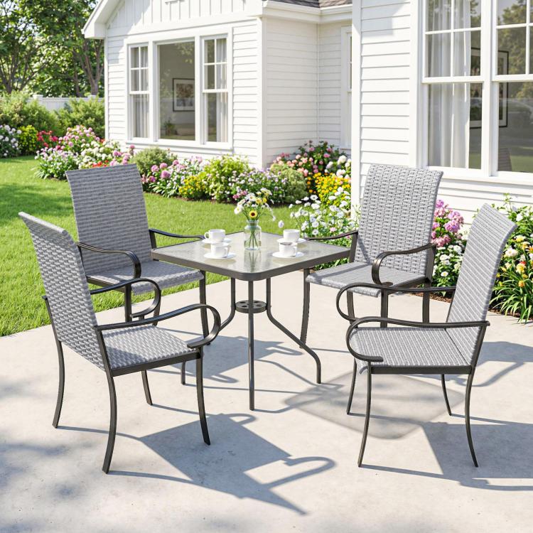 Four gray outdoor wicker dining chairs with a round glass table on a patio