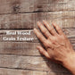 Gray faux wood plank texture with raised grain detail and a hand pressing the surface.