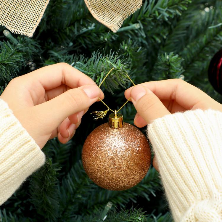 Hands placing a brown glitter ornament on a green Christmas tree branch