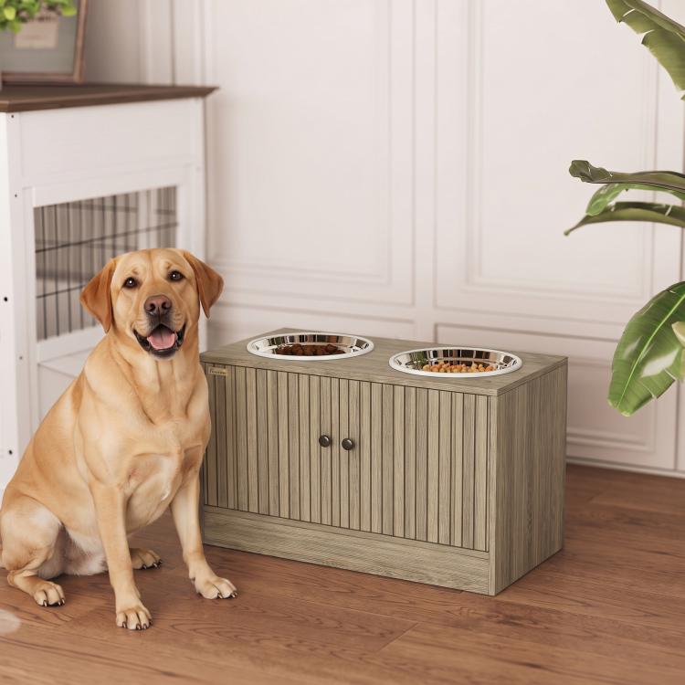 Dog sitting beside wood-grain elevated feeding cabinet with two stainless bowls