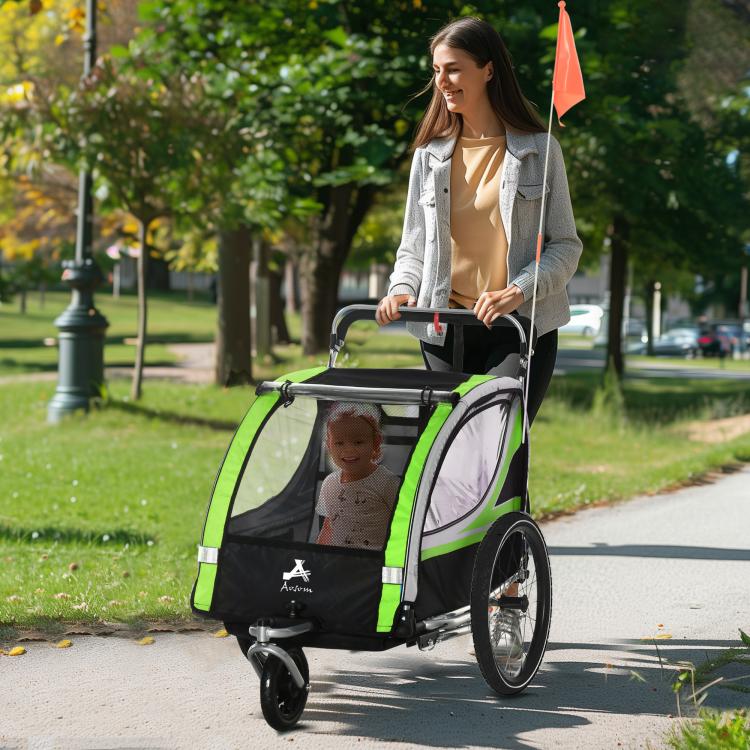 Green and black jogging stroller-style trailer with orange flag and two children in padded seats