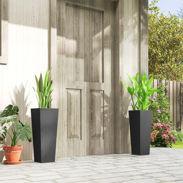 Two black tall woven planters with potted plants in a courtyard beside a wall