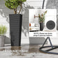 Tall black plastic planter with rattan-style texture beside indoor plant display