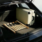 Bamboo luggage rack with black straps, placed in a car trunk to support a suitcase