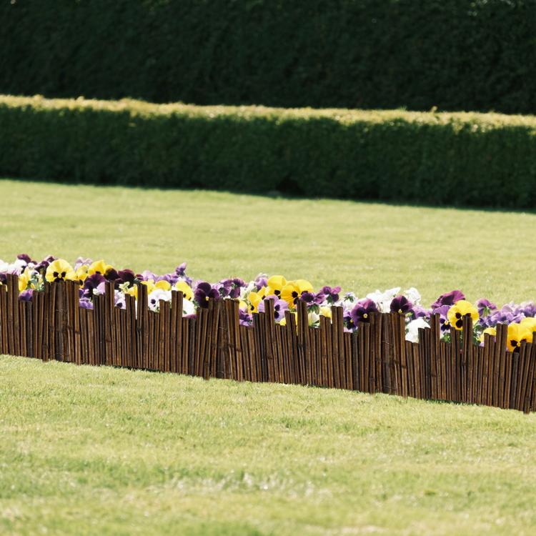 Dark bamboo fence edging with upright poles bordering a lawn