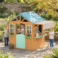 Wooden outdoor playhouse with blue roof, front windows, mint half door, and striped awning