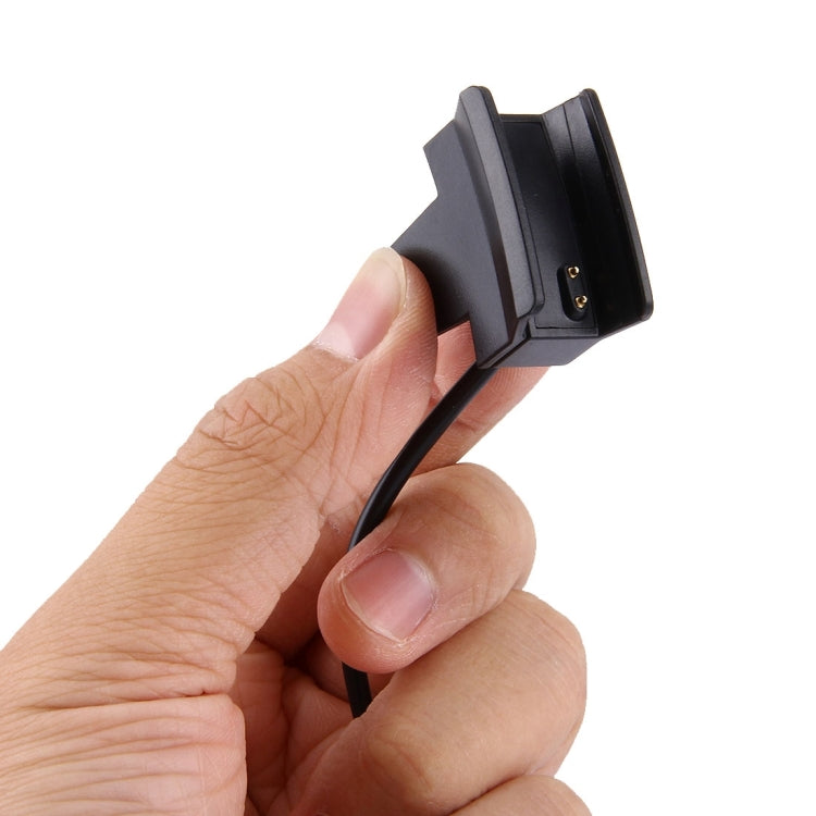Hand holding a black charging clip for Fitbit Alta watch with attached cable