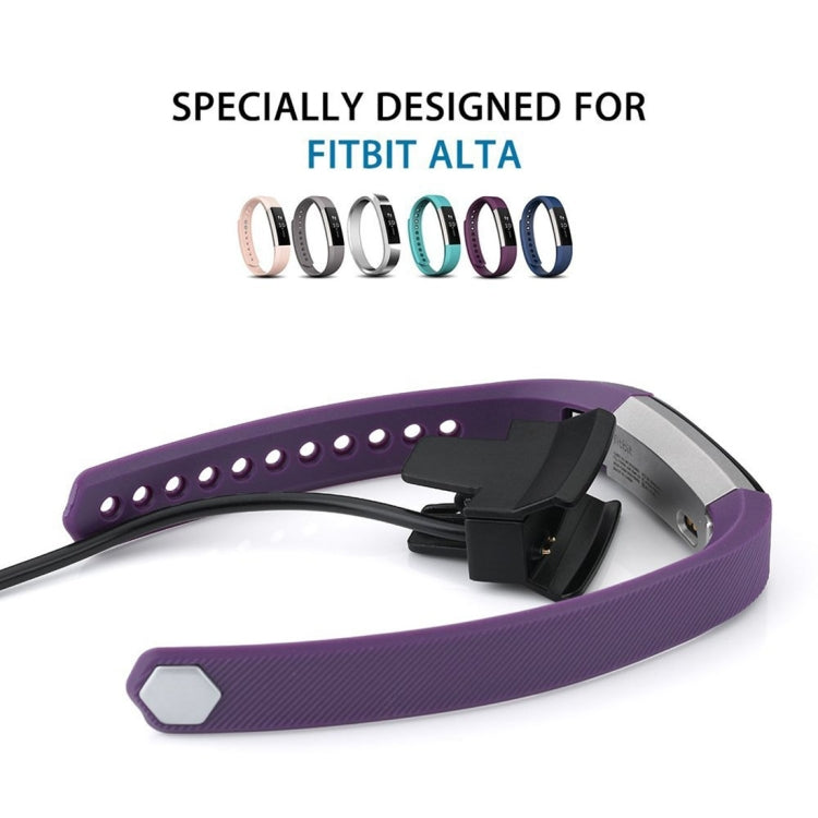 Purple Fitbit Alta watch with black charging clip dock connected to USB cable