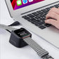 Black charging dock stand charging a smartwatch with braided strap by laptop