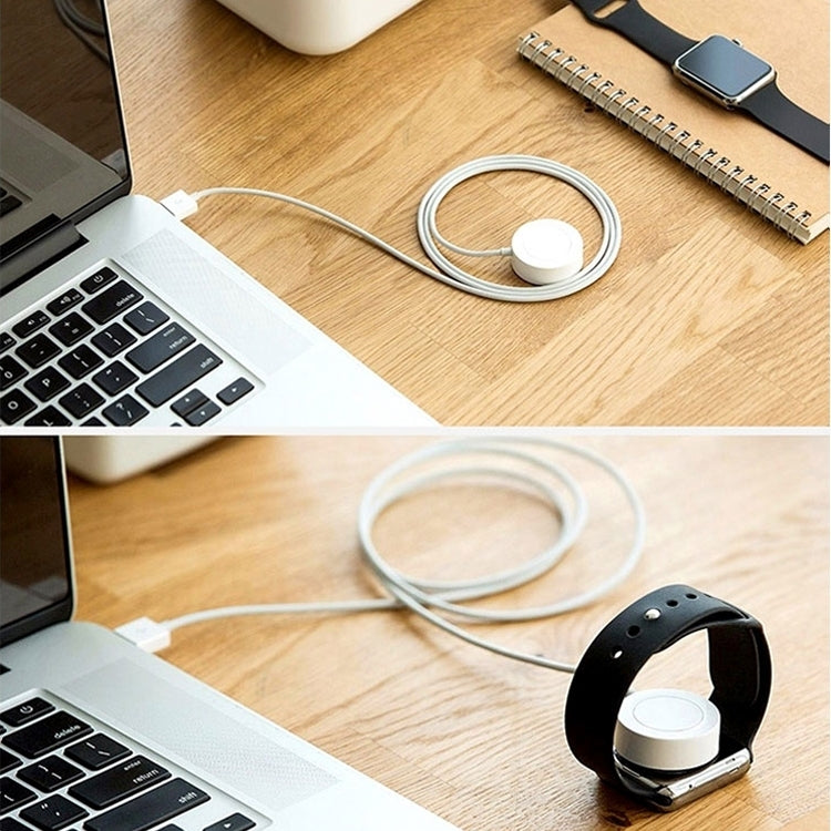 White magnetic watch charging cable with round puck on a wooden desk