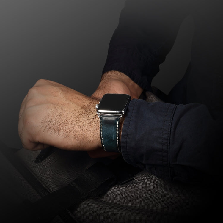 Dark blue leather watch band on wrist with metal buckle and stitched perforated strap