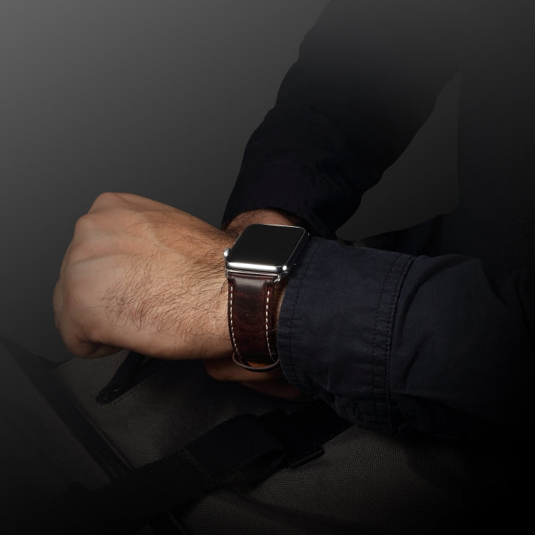 Dark brown leather watch band worn on wrist with metal buckle and stitched holes