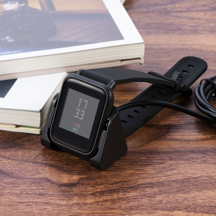 Smart watch charging on black cradle with connected USB cable on wood surface