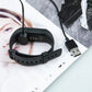 Black smartwatch charging cradle cable attached to a fitness watch band