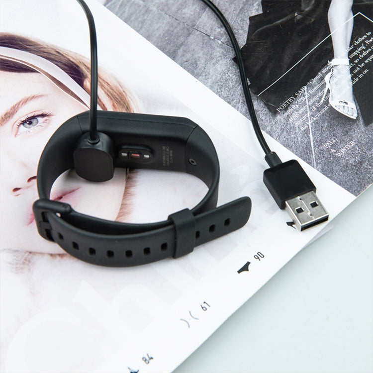 Black smartwatch charging cradle cable attached to a fitness watch band