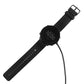 Smartwatch with black perforated band and charging cable connected to dock puck