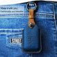 Blue leather key fob cover on denim with embossed button panel and keyring