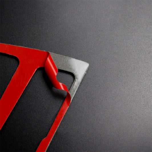 Carbon fiber-look trim piece with textured black weave and red protective backing