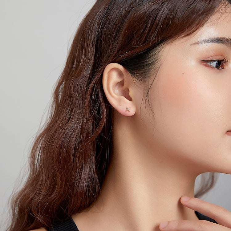 Woman wearing gold star stud earrings with a small round CZ stone at the ear.