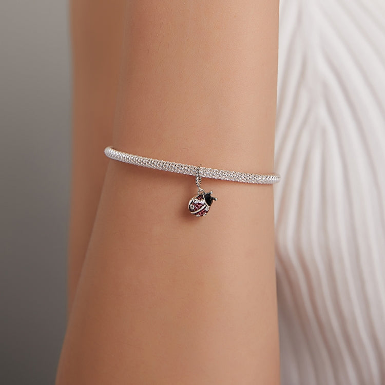 Silver snake-chain bracelet on wrist with small ladybug pendant charm in red and black