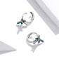 Pair of sterling silver dragonfly ear studs with blue wings, green accents, and pink center stone